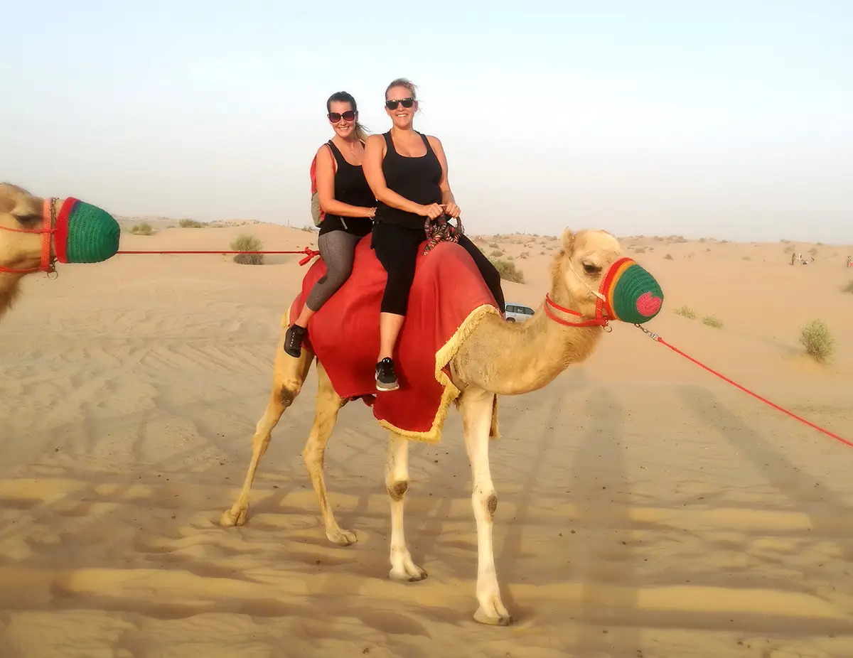 Two friends sit atop a camel in Dubai
