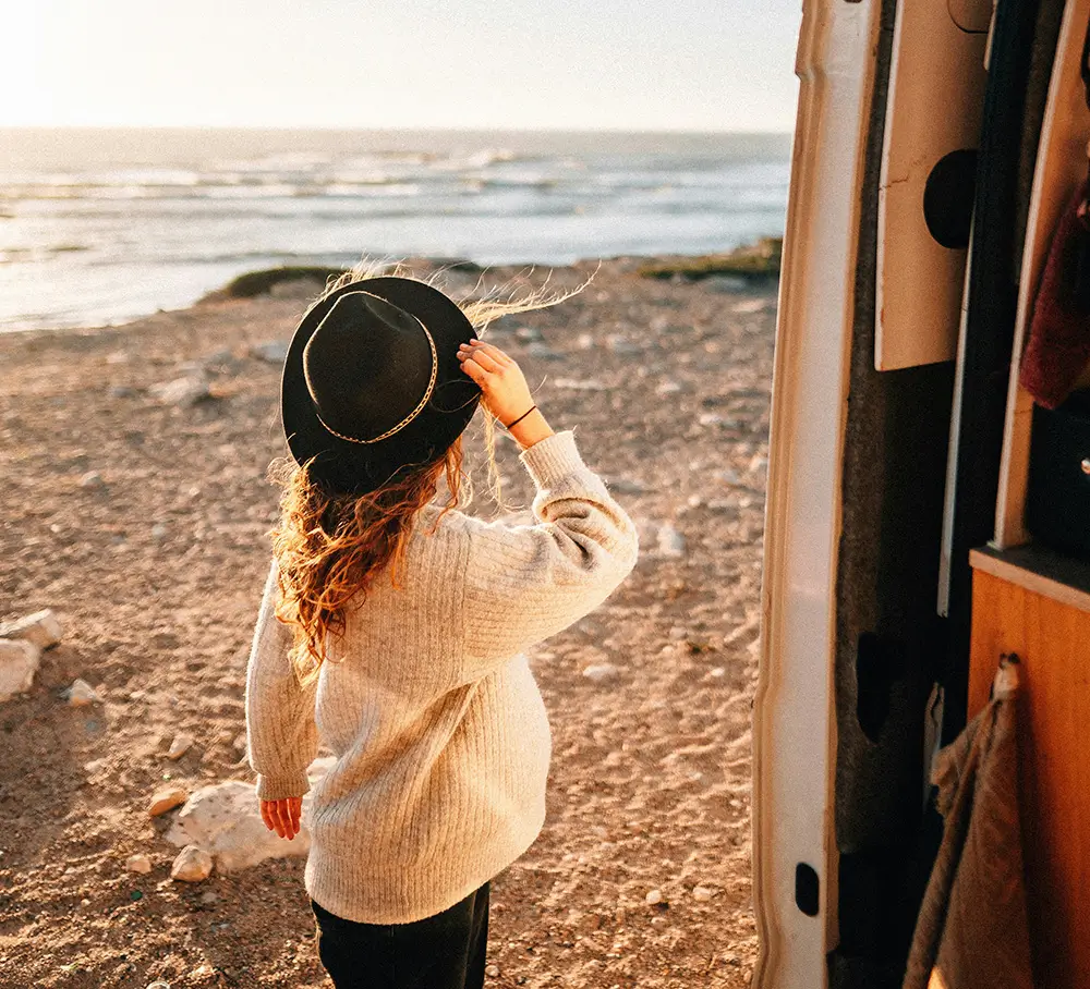 A person stands at a beach, in front of a motorhome