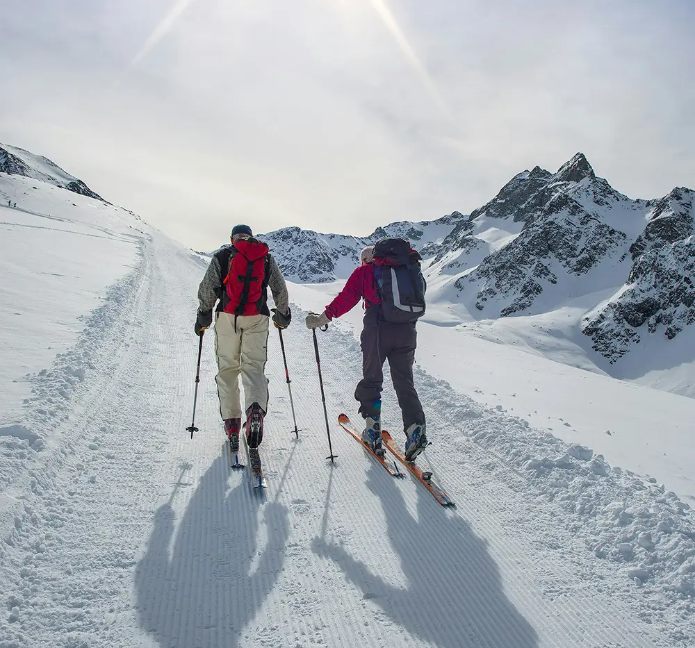 Two people wearing skis, climbing a snowy path