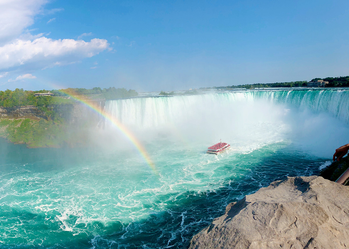 View of the Niagara Falls, with a boat in the rapids and a rainbow arcing into the water