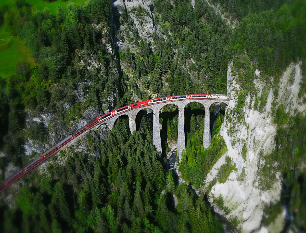 A train travelling across a high train bridge against a backdrop of steep hills