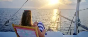 Lydia sitting on a deck chair on a boat, watching the sun set across calm waters
