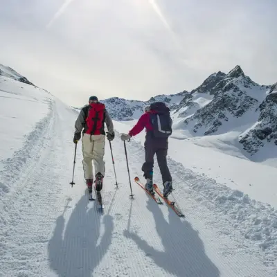 Two people wearing skis, climbing a snowy path